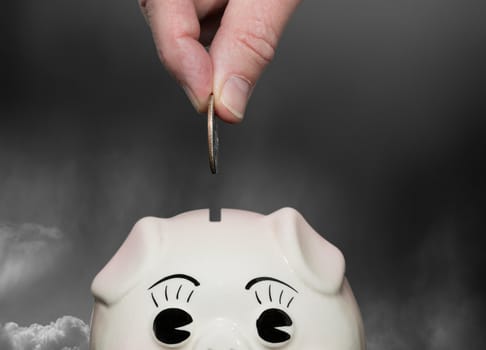 Coin being inserted into piggy bank with fingers suggesting saving for a rainy day or stormy weather