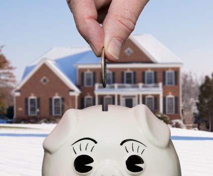 Coin being inserted into piggy bank with fingers suggesting saving for a deposit or mortgage on a home