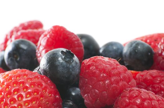 Macro image with selective focus on a strawberry, blueberry and raspberry in the foreground with more fruit in the background with copy space at the top with white background.