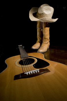 Spotlight on guitar in the foreground with selective focus and cowboy boots in the background