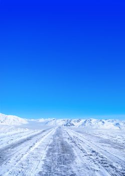 Snow covered road in winter with mountains in the distance