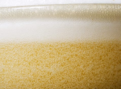 Macro shot of the top of a glass of beer with lots of foam and bubbles.