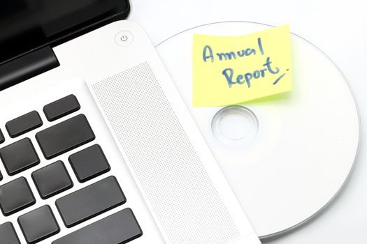 White laptop with Business Annual Report dvd disk in slot-loading drive on a white background.