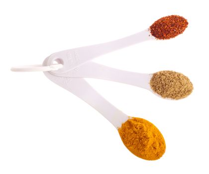 indian spices in measuring spoons (curcuma, coriander, red pepper flakes) isolated on white background