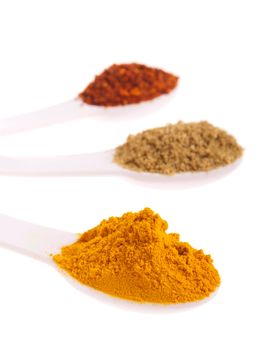 indian spices in measuring spoons (curcuma, coriander, red pepper flakes) isolated on white background (shallow DOF, focus on first)