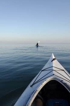 Two kayaks on the lake with the woman paddling in the distance on a calm evening