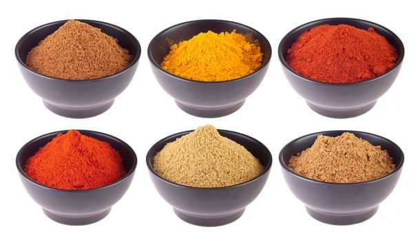 collection of indian spices (cumin, coriander, paprika, garam masala, curcuma, chili powder) on black ceramic cups isolated on white background