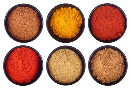 collection of indian spices (cumin, coriander, paprika, garam masala, curcuma, chili powder) on black ceramic cups isolated on white background