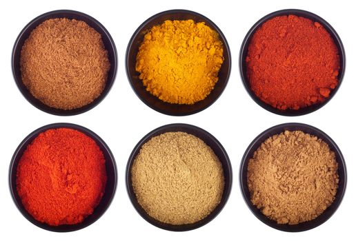 collection of indian spices (cumin, coriander, paprika, garam masala, curcuma, chili powder) on black ceramic cups isolated on white background