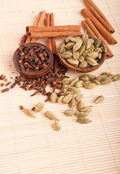 gorgeous setting with cooking spices and herbs (cloves, cardamom pods, cinnamon sticks) on a wooden mat