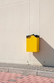 yellow garbage can hanging on wall at a urban sidewalk