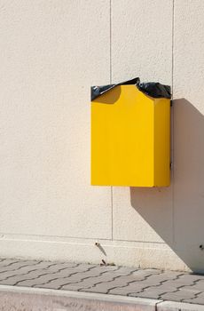 yellow garbage can hanging on wall at a urban sidewalk