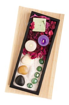 gorgeous spa setting with candles, stones, sand, rake, incense and dry petal roses on a black tray and wooden mat (isolated on white background)