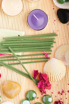 gorgeous spa setting with candles, stones, seashells, incense and dry petal roses on a wooden mat (close up picture)