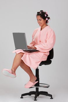 Image of a young woman with hair curlers working on a laptop.