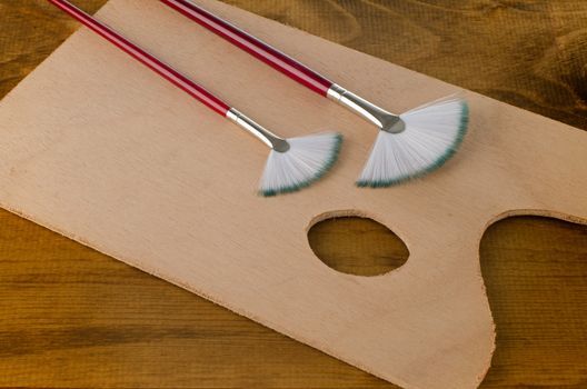 Painting brushes and art pallete on wooden board.