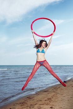 Smiling lady with red hoop jumping at the beach