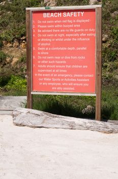 wooden beach safety sign with a big list of rules (at a white sandy beach)