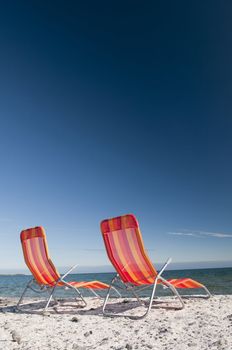 Lounging beach chairs on the Lake Ontario shoreline with large copy space area in the deep blue sky