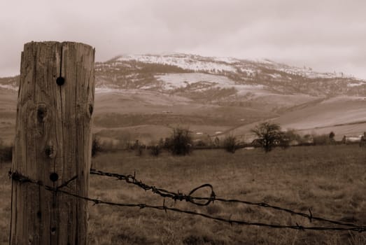 Sepia toned closeup on fencepost with wire, hills in background