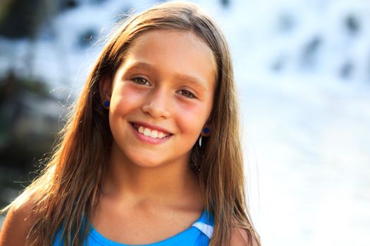 Portrait of a young gir lwith the sun shining on the side ofher face.  She is staning on the River bank with waterfalls out of focus behind her in the background.