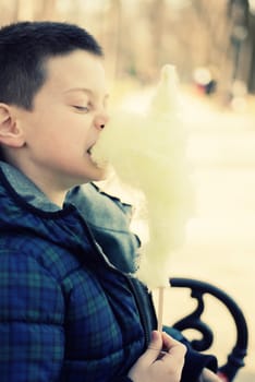 Boy bitting a sugarwool chunk in a sunny park