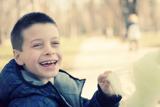 Happy young boy eating sugarwool in a park