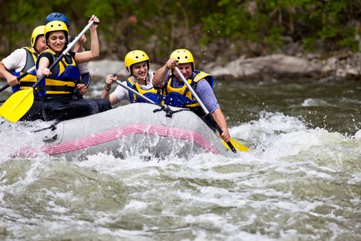 Group of five people whitewater rafting and rowing on river