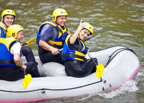 Group of four happy people sitting on a boat, woman showing rock on sign