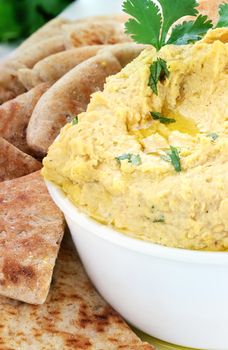 Bowl of hummus topped with pure olive oil and cilantro and served with wedges of pita bread for a healthy snack.