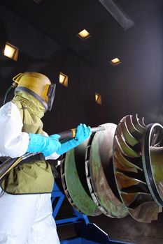 A worker sandblasting paint from a product