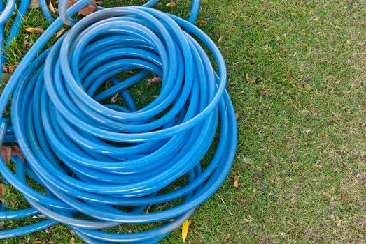 Blue garden water hose stack together on the left with green grass background