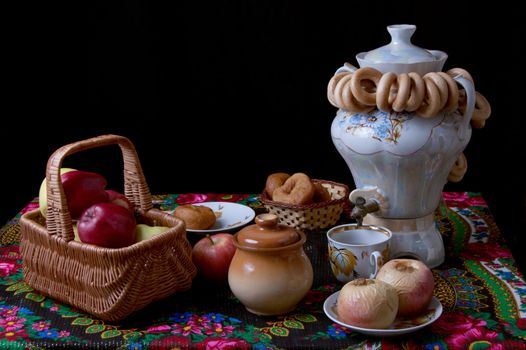 Samovar with bagels and apples on table over black