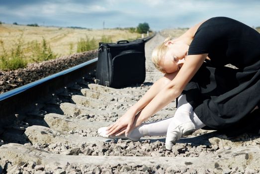 Tired ballet dancer sitting on the railway and waiting for a train