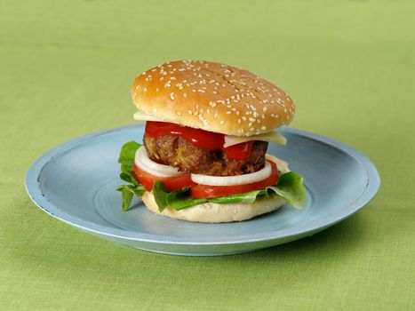 Photo of a hamburger on a blue plate resting on a green table cloth.

