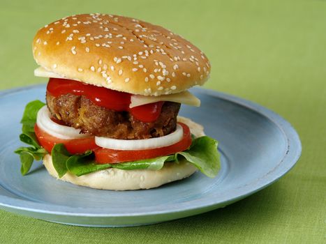 Photo of a hamburger on a blue plate resting on a green table cloth.
