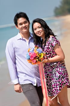 lovely young couple with flower bouquet standing on the beach