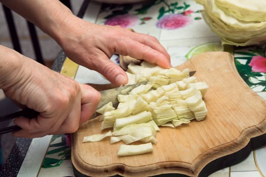 The woman cuts cabbage on a table