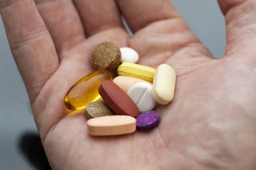 An open mans hand with a cocktail of various tablets and pills, drugs and supplements.