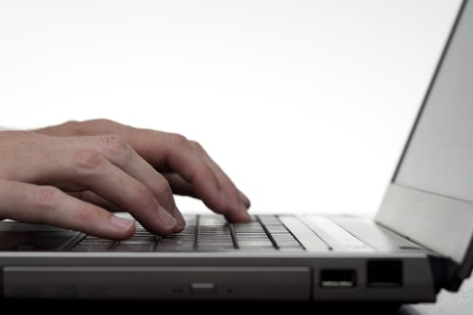 Closeup low angle image of a mans hands typing on a laptop keyboard against white