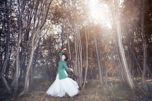 Elegant lady in the green coat and wedding dress dancing in the wild forest. Natural light and colors