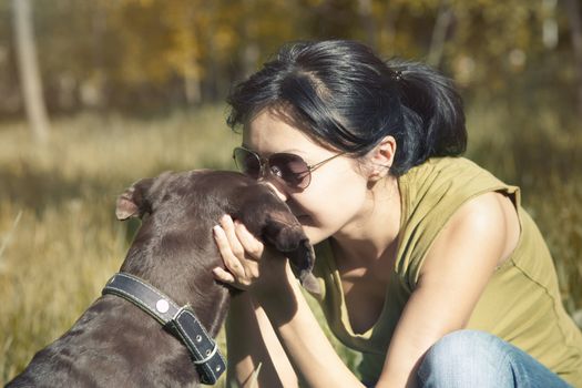 Happy lady outdoors kissing and pampering her dog. Spring sunlight used and cross-processed colors added