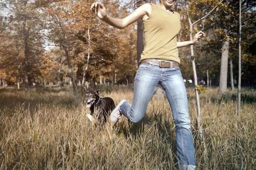 Happy young girl outdoors running with dog in the autumn forest