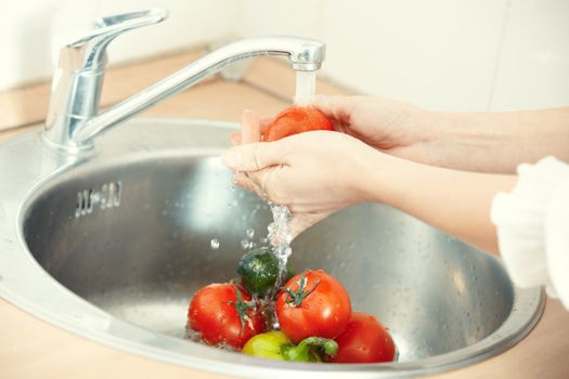 Hands of woman washing vegetables at her kitchen