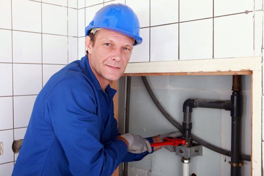 Plumber installing pipes with a large wrench