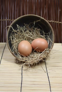 Two fresh brown eggs in a nest of straw in a round bowl, on a bamboo mat. Set on a portrait format with copy-space available.
