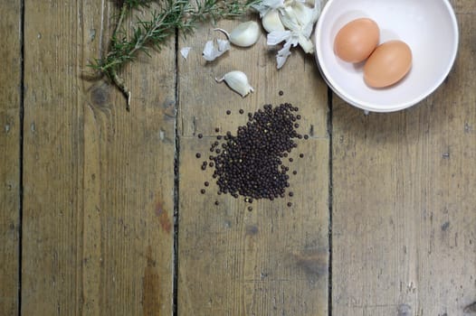 Kitchen ingredients comprising of brown eggs, garlic, fresh rosemary and black lentils. All set on a landscape format against a wooden background with plenty of copy-space available.