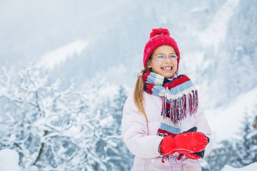 Smiling happy girl having fun outdoors on snowing winter day in Alps playing in snow.