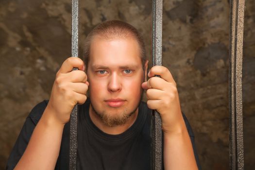 Young man looking from behind the bars