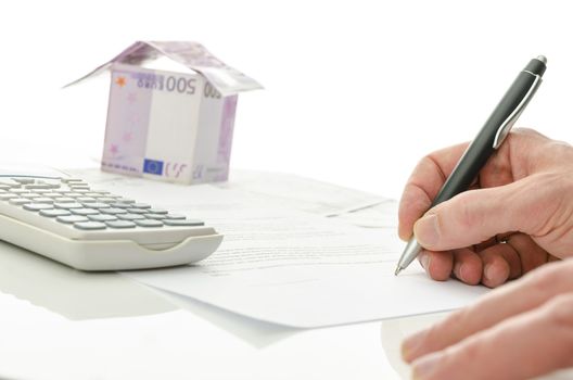 Contract signing of house sale with money house in the background. On a white table.